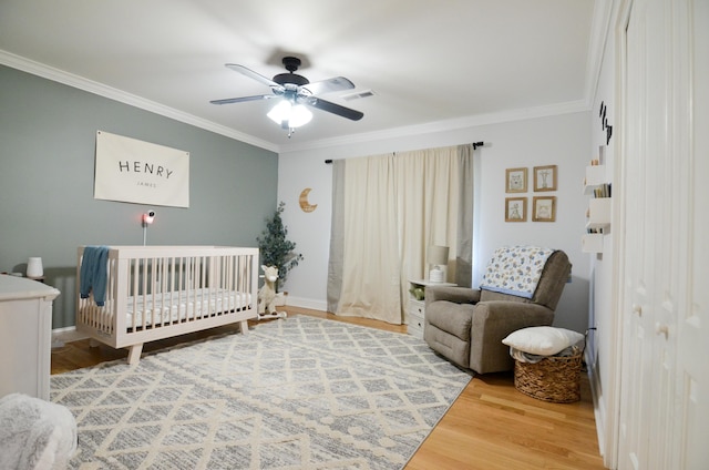 bedroom featuring ceiling fan, crown molding, a crib, and hardwood / wood-style flooring