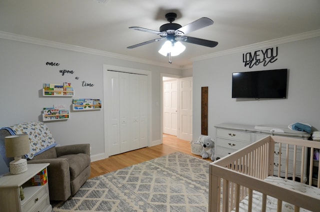 bedroom with ceiling fan, light wood-type flooring, ornamental molding, a crib, and a closet