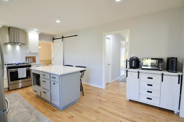 kitchen featuring white cabinetry, wall chimney range hood, a barn door, stainless steel range with electric stovetop, and a kitchen island