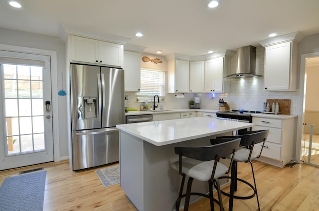 kitchen featuring wall chimney exhaust hood, stainless steel appliances, a center island, light hardwood / wood-style floors, and white cabinetry