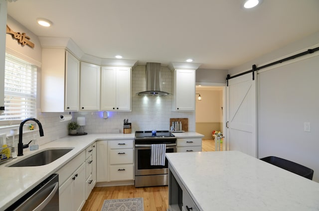 kitchen with sink, wall chimney exhaust hood, a barn door, backsplash, and appliances with stainless steel finishes