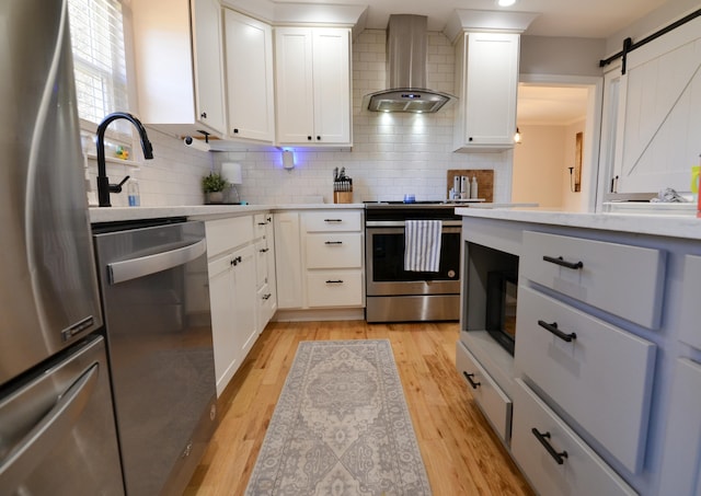 kitchen with white cabinetry, wall chimney exhaust hood, stainless steel appliances, tasteful backsplash, and a barn door