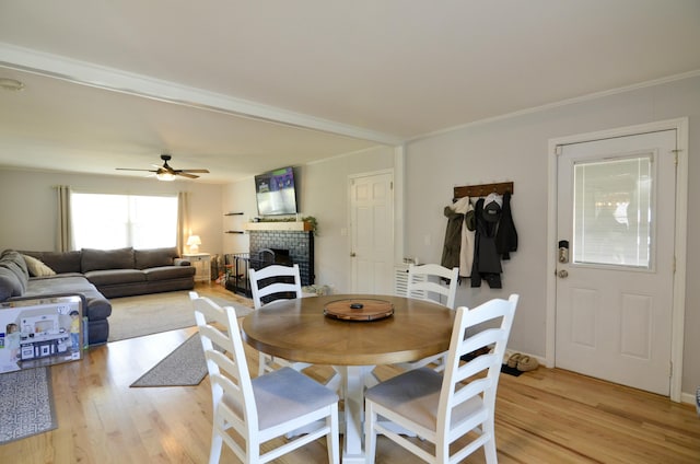 dining area with a tile fireplace, ceiling fan, ornamental molding, and light wood-type flooring