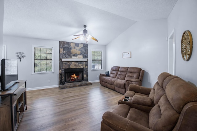 living room with ceiling fan, hardwood / wood-style floors, a textured ceiling, vaulted ceiling, and a fireplace