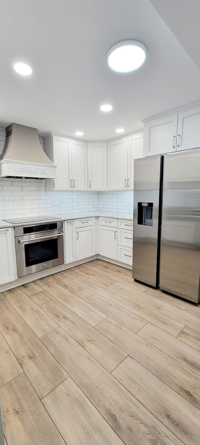 kitchen featuring custom exhaust hood, white cabinets, decorative backsplash, light hardwood / wood-style floors, and stainless steel appliances