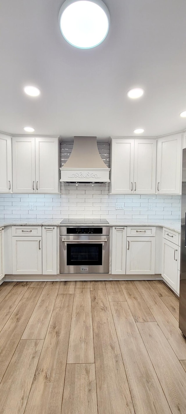 kitchen with custom exhaust hood, stainless steel oven, decorative backsplash, and white cabinetry