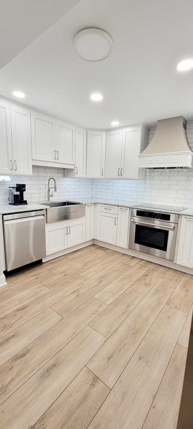 kitchen featuring custom exhaust hood, sink, light wood-type flooring, white cabinetry, and stainless steel appliances