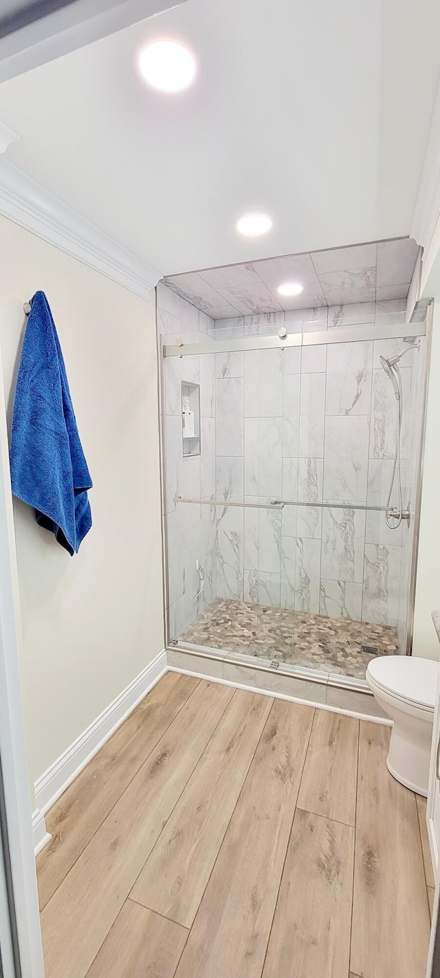 bathroom featuring toilet, a shower with shower door, and ornamental molding