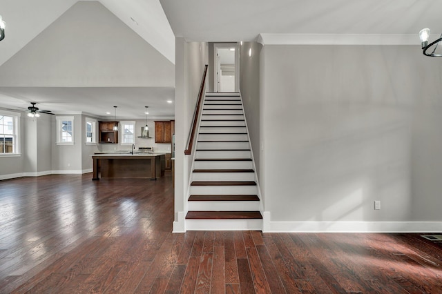 stairs featuring sink, a high ceiling, hardwood / wood-style flooring, ceiling fan with notable chandelier, and ornamental molding