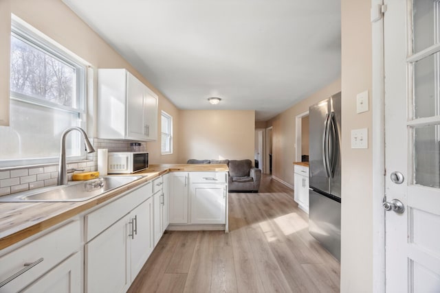 kitchen featuring wooden counters, white cabinets, sink, stainless steel fridge, and kitchen peninsula