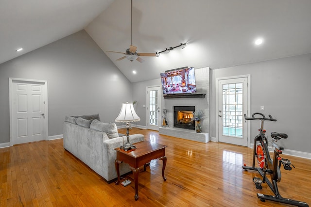 living room with track lighting, wood-type flooring, ceiling fan, high vaulted ceiling, and a brick fireplace