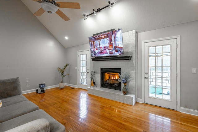 living room with a brick fireplace, wood-type flooring, ceiling fan, and vaulted ceiling