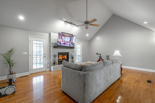 living room with a wealth of natural light, a brick fireplace, light hardwood / wood-style floors, and high vaulted ceiling