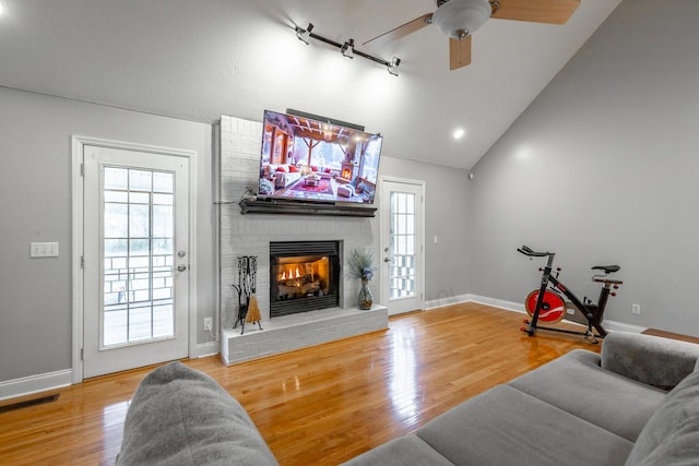 living room featuring wood-type flooring, ceiling fan, a fireplace, and lofted ceiling