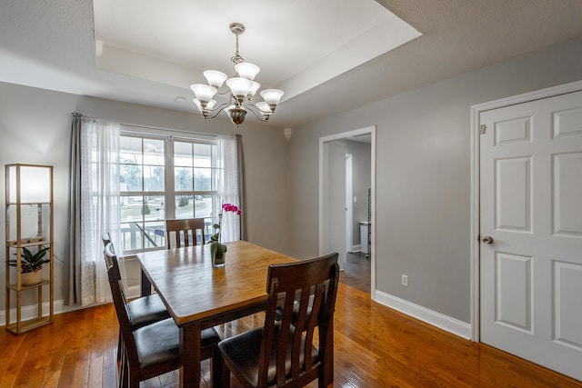 dining area with an inviting chandelier, dark hardwood / wood-style floors, and a tray ceiling