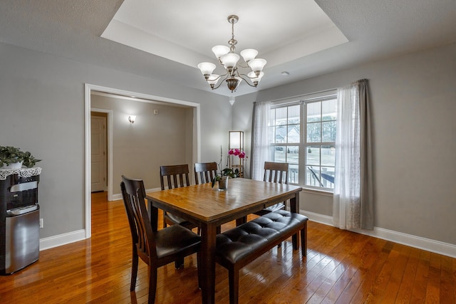 dining space with hardwood / wood-style flooring, a chandelier, and a tray ceiling