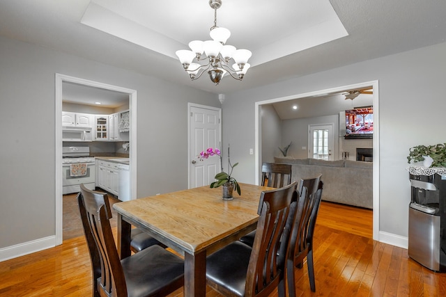 dining space featuring a large fireplace, a tray ceiling, a notable chandelier, and light wood-type flooring