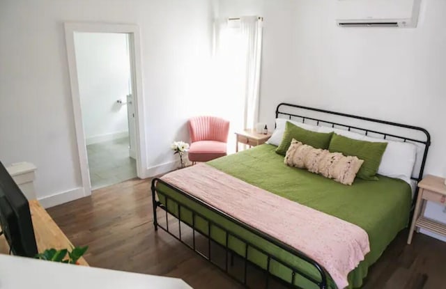 bedroom with connected bathroom, dark hardwood / wood-style floors, and a wall mounted AC