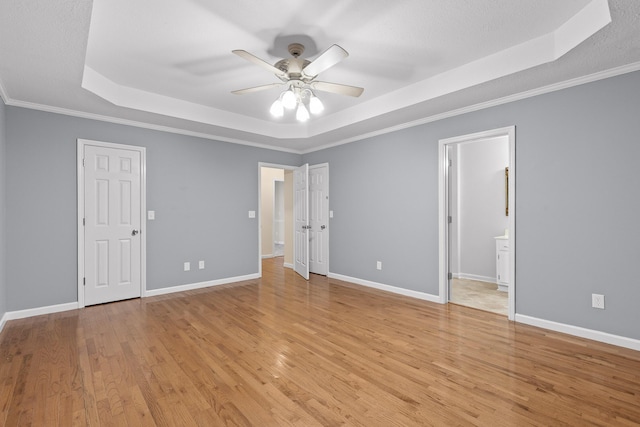 unfurnished bedroom with ceiling fan, crown molding, ensuite bathroom, light hardwood / wood-style floors, and a tray ceiling