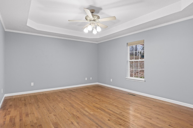 unfurnished room with ceiling fan, a raised ceiling, ornamental molding, and light hardwood / wood-style flooring