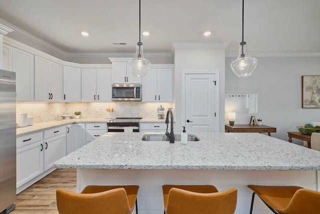 kitchen with stainless steel appliances, a kitchen island with sink, sink, decorative light fixtures, and white cabinets