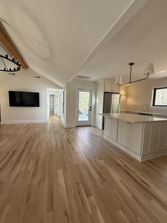 unfurnished living room with vaulted ceiling with beams, plenty of natural light, and light hardwood / wood-style floors