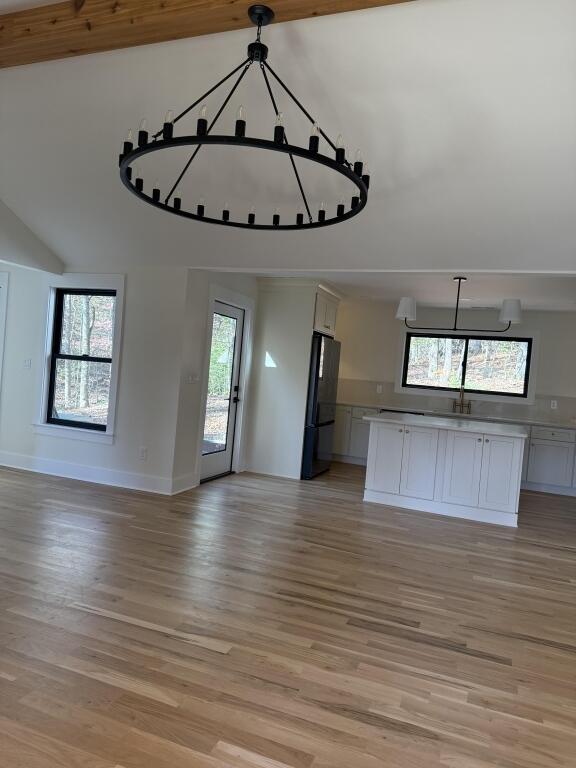 unfurnished living room featuring beam ceiling, light wood-type flooring, high vaulted ceiling, and plenty of natural light