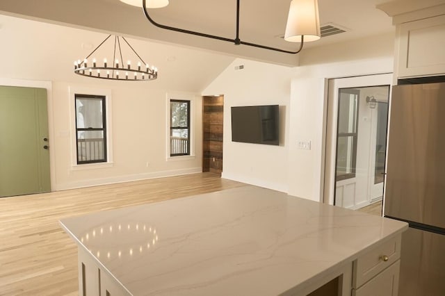 kitchen featuring light stone counters, stainless steel fridge, hanging light fixtures, and light wood-type flooring