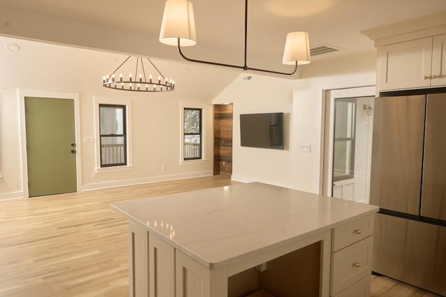 kitchen with stainless steel refrigerator, white cabinetry, a center island, light stone counters, and decorative light fixtures