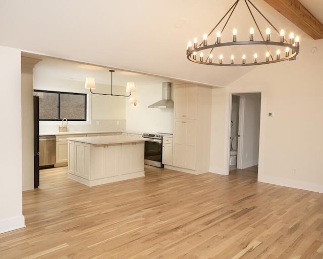 kitchen with a center island, hanging light fixtures, appliances with stainless steel finishes, beam ceiling, and wall chimney range hood