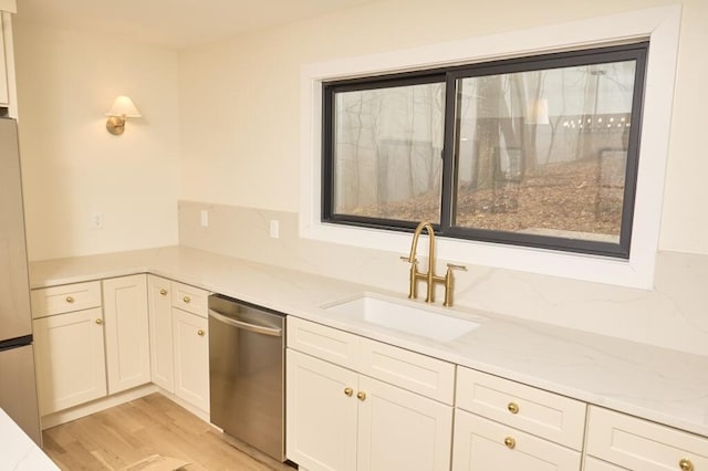 kitchen featuring sink, dishwasher, light stone counters, light hardwood / wood-style floors, and white cabinets