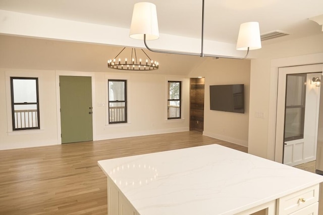 kitchen with white cabinetry, an inviting chandelier, light stone counters, decorative light fixtures, and light wood-type flooring