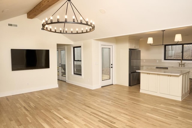 kitchen featuring a kitchen island, vaulted ceiling with beams, stainless steel refrigerator, and decorative light fixtures