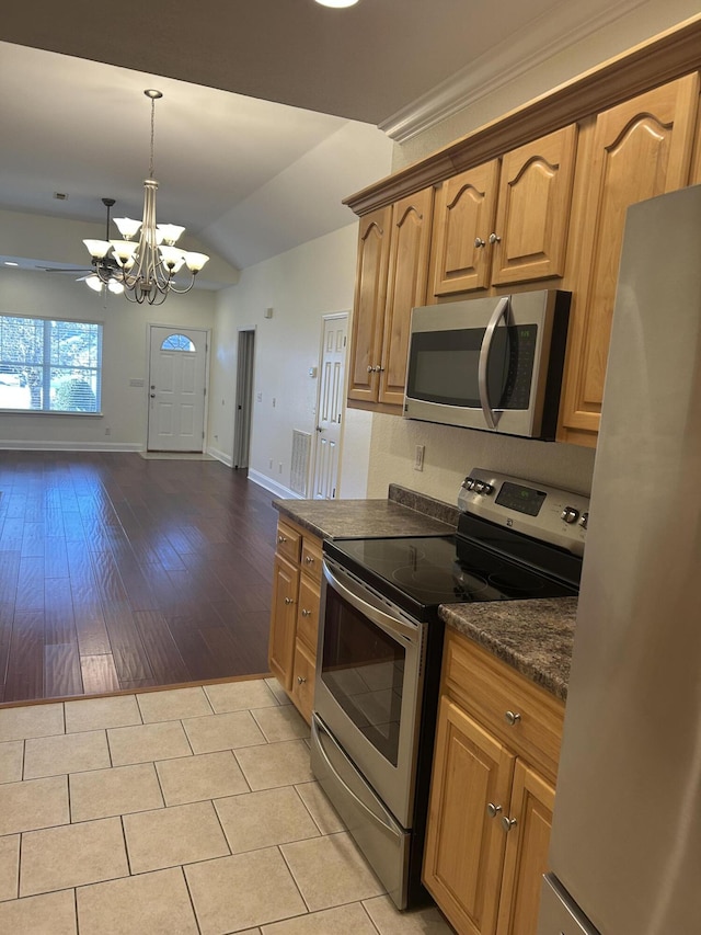 kitchen with hanging light fixtures, vaulted ceiling, dark stone countertops, appliances with stainless steel finishes, and light hardwood / wood-style floors