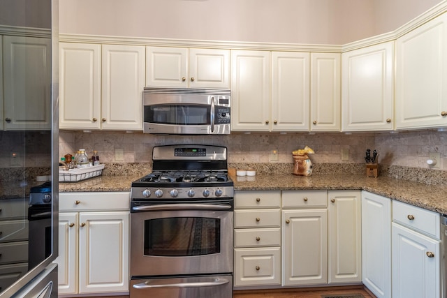 kitchen featuring stainless steel appliances, white cabinets, tasteful backsplash, and dark stone counters