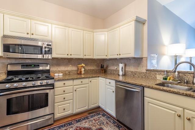 kitchen with appliances with stainless steel finishes, tasteful backsplash, stone countertops, and sink