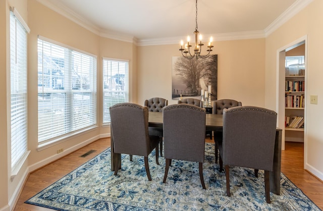 dining room featuring a notable chandelier, crown molding, wood-type flooring, and plenty of natural light