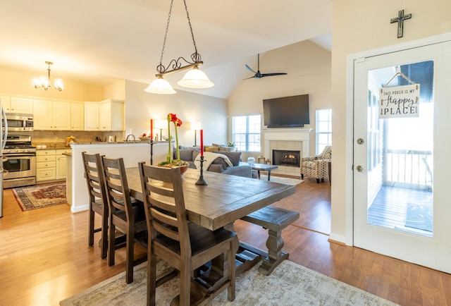 dining room featuring lofted ceiling, a fireplace, light hardwood / wood-style floors, and ceiling fan with notable chandelier