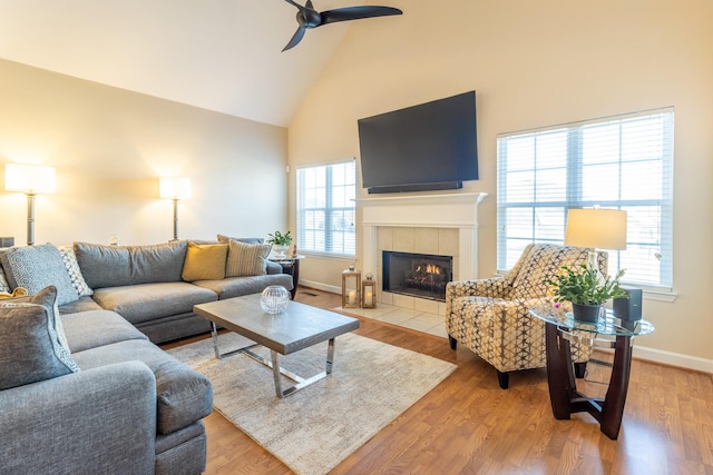 living room with high vaulted ceiling, a tiled fireplace, ceiling fan, and light hardwood / wood-style flooring