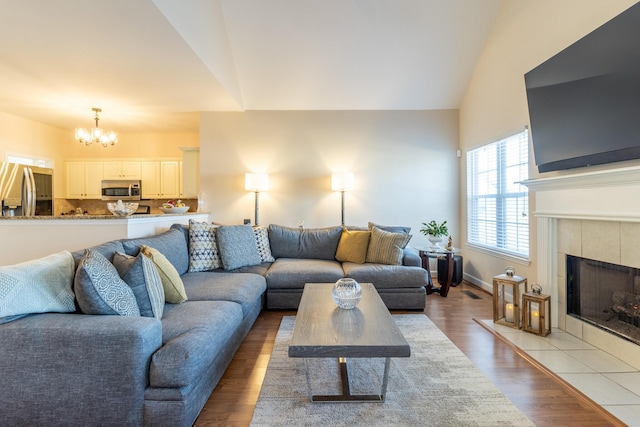 living room featuring lofted ceiling, a fireplace, an inviting chandelier, and light hardwood / wood-style flooring