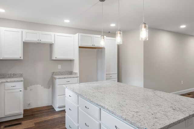 kitchen with light stone counters, a kitchen island, pendant lighting, dark hardwood / wood-style floors, and white cabinetry