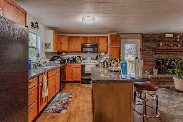 kitchen with sink, black appliances, light hardwood / wood-style floors, a kitchen bar, and wood ceiling