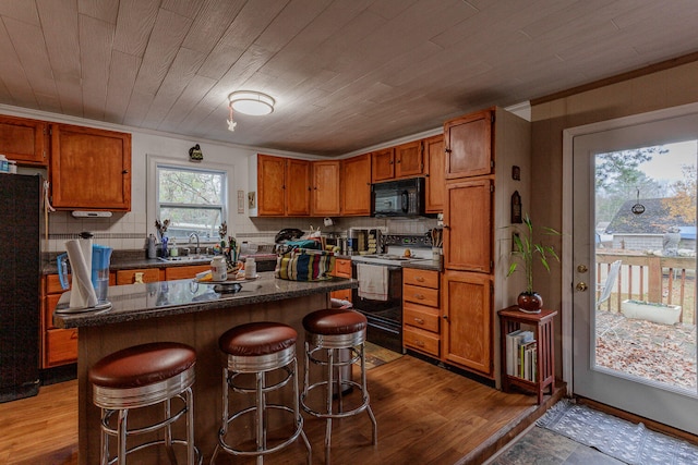 kitchen with wood ceiling, a breakfast bar, sink, black appliances, and a center island