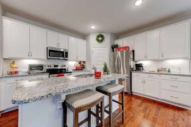 kitchen featuring white cabinets, appliances with stainless steel finishes, a center island with sink, and wood-type flooring