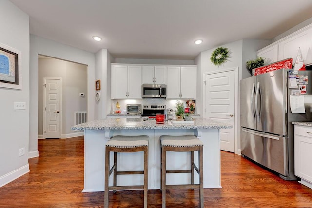 kitchen with a kitchen breakfast bar, stainless steel appliances, a center island with sink, dark hardwood / wood-style floors, and white cabinetry