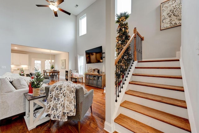 living room with plenty of natural light, a high ceiling, ceiling fan with notable chandelier, and wood-type flooring