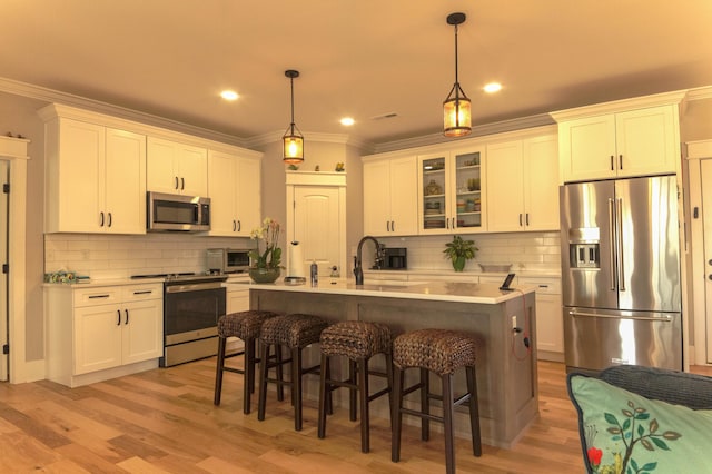 kitchen with an island with sink, light wood-type flooring, decorative light fixtures, and appliances with stainless steel finishes