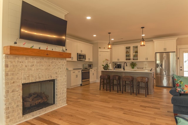 kitchen featuring white cabinetry, stainless steel appliances, hanging light fixtures, and an island with sink