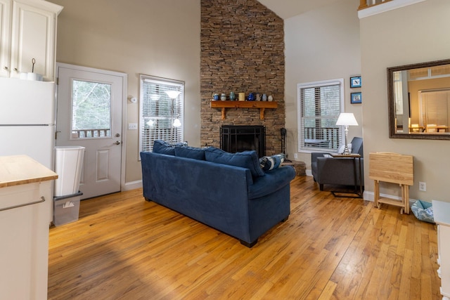 living room featuring a high ceiling, a healthy amount of sunlight, a stone fireplace, and light hardwood / wood-style floors