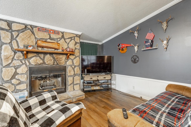 living room with a textured ceiling, vaulted ceiling, crown molding, hardwood / wood-style flooring, and a stone fireplace